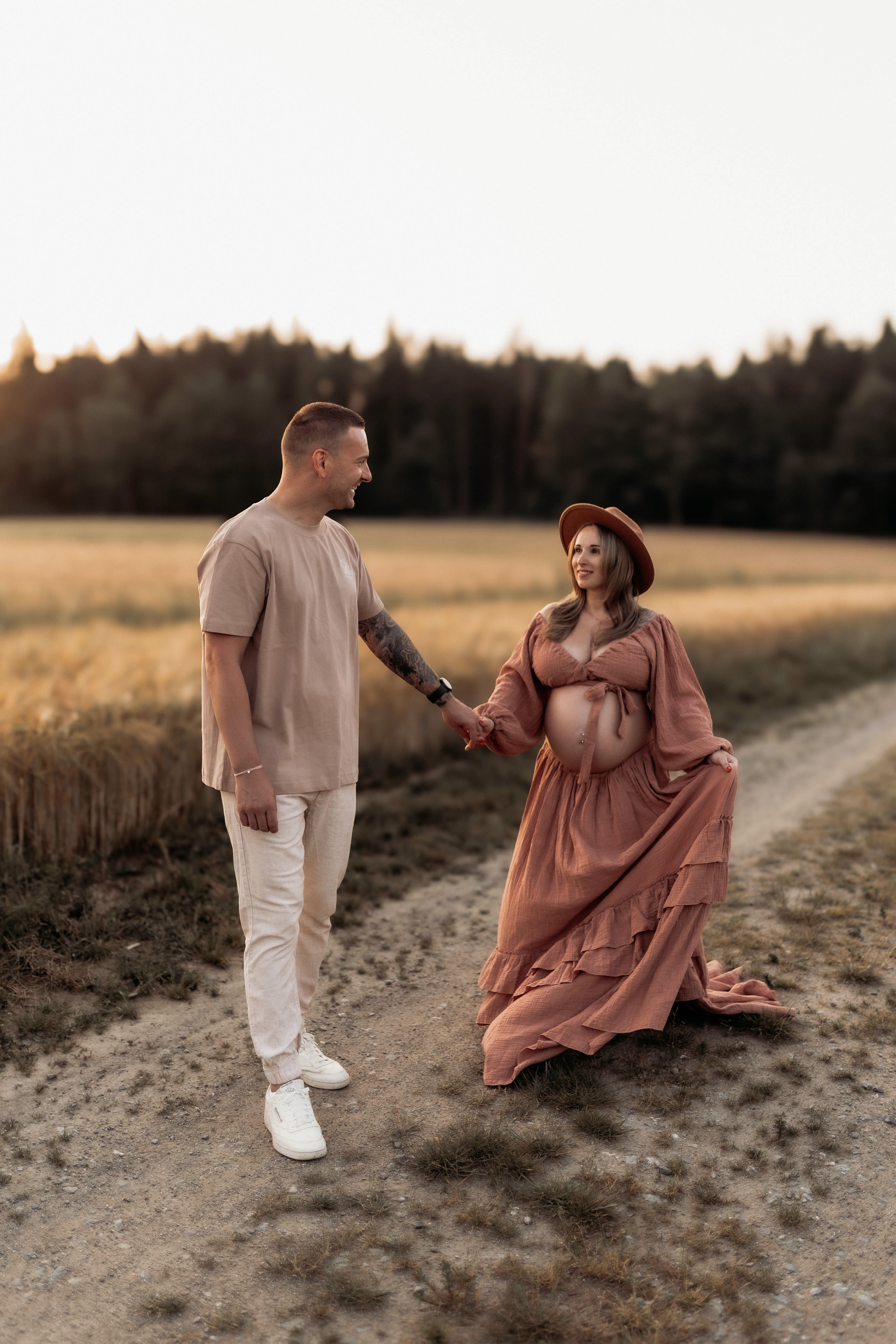 Schwangeres Paar geht Hand in Hand einen Feldweg entlang im warmen Abendlicht -- Babybauch-Shooting von Simple Moments