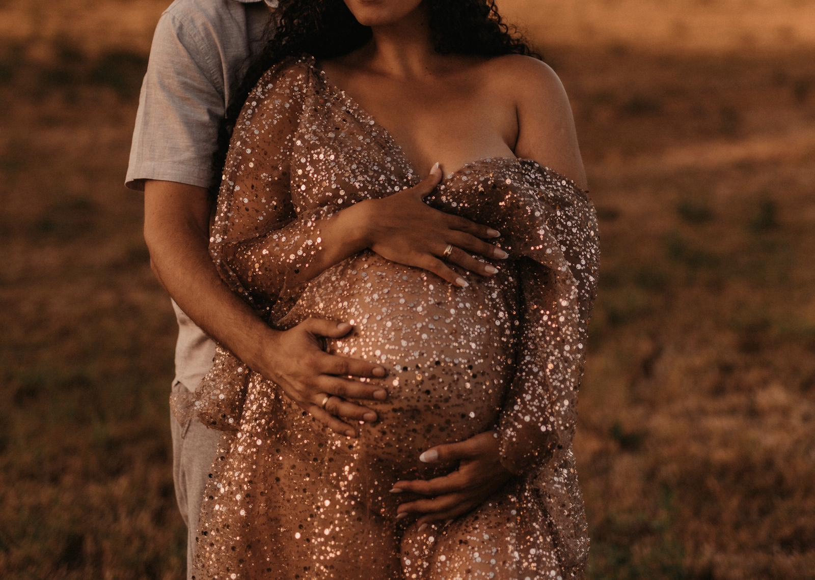 Babybauch im glitzernden Paillettenkleid, die Hände beider Eltern liegen darauf