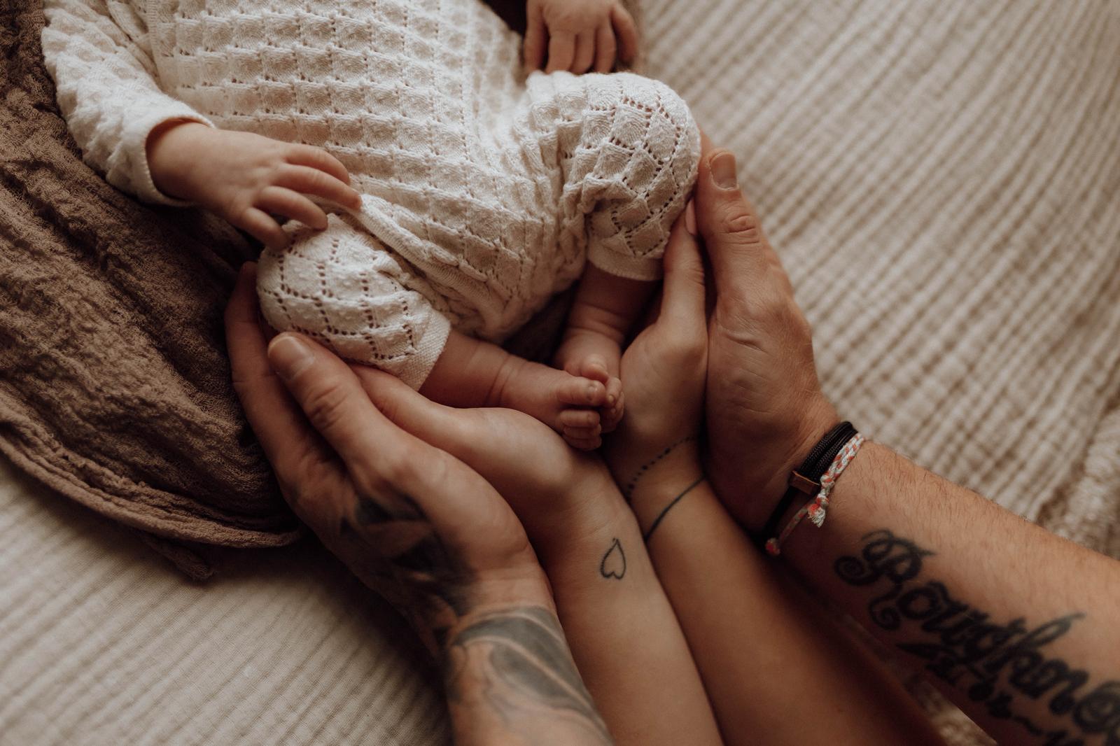 Elternhände halten liebevoll ihr Neugeborenes