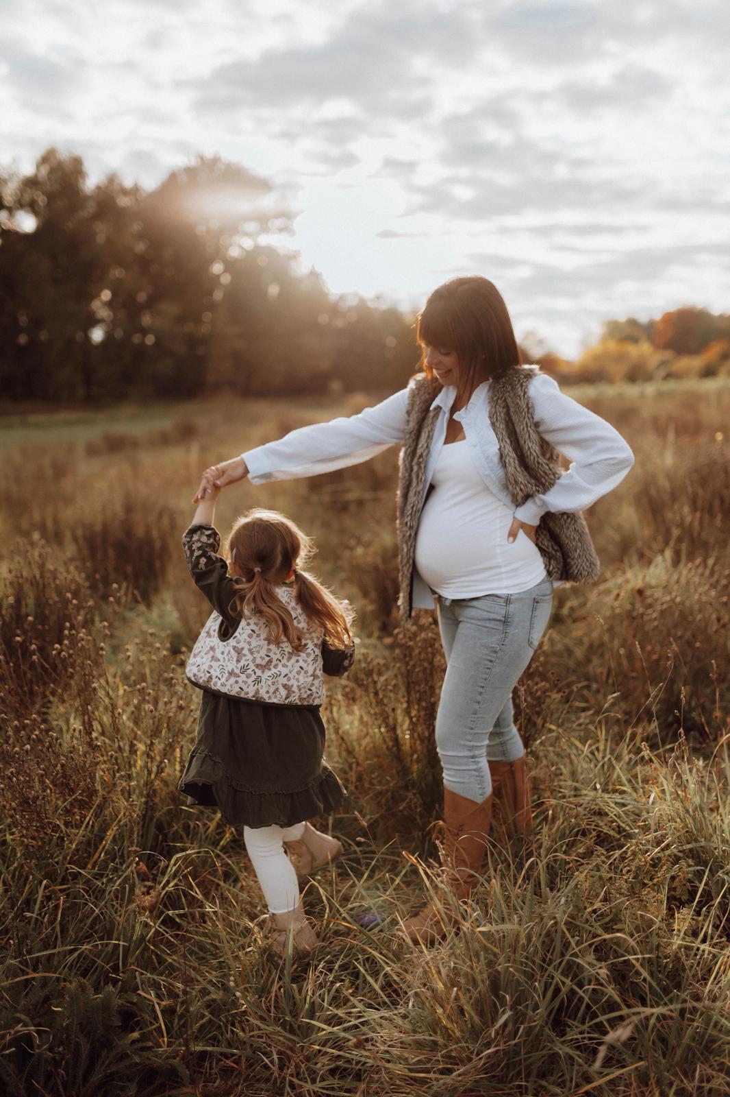 Schwangere Mama tanzt mit ihrer Tochter auf einer Wiese im Abendlicht