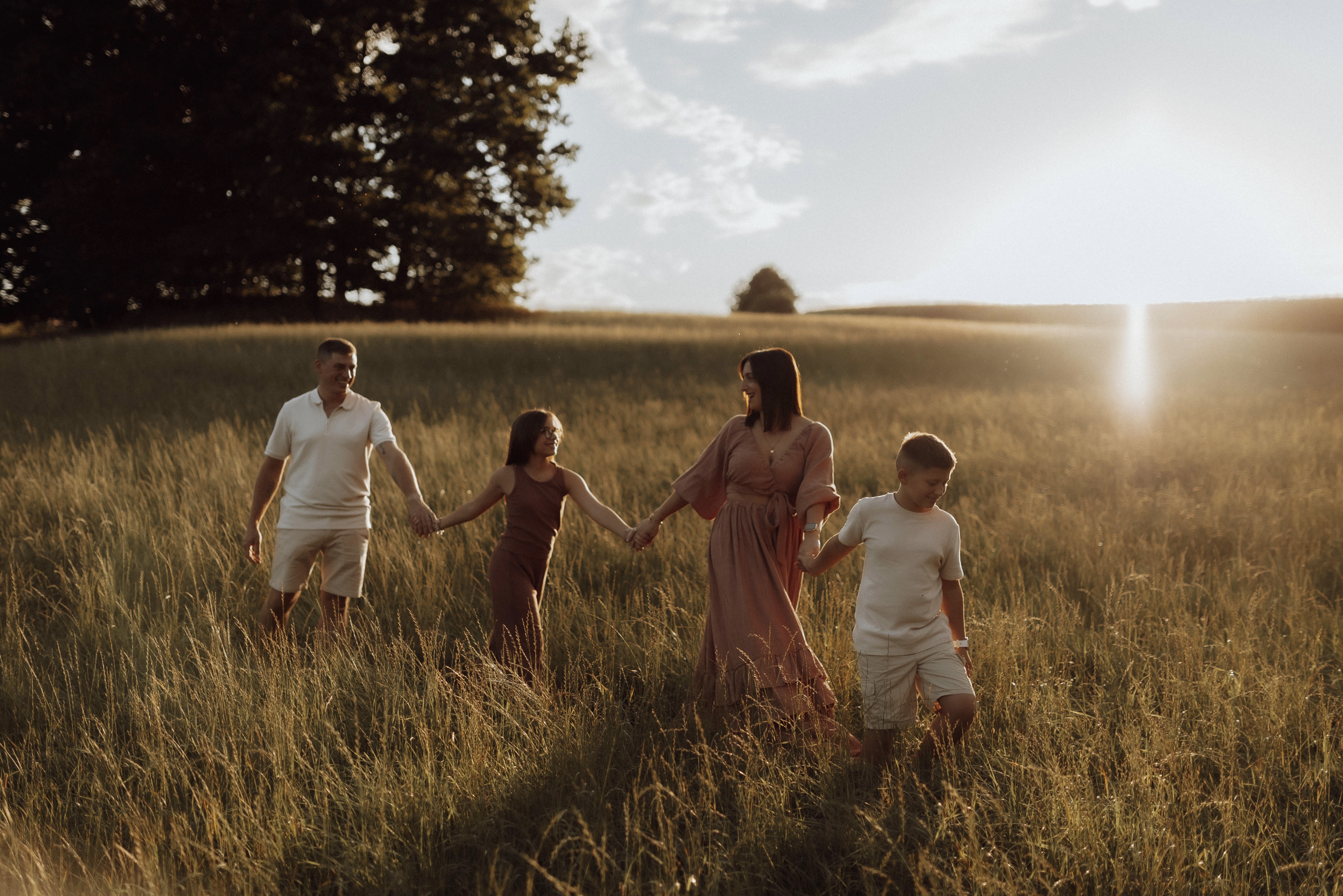 Familie spaziert Hand in Hand über eine goldene Wiese im warmen Abendlicht -- emotionale Familienfotografie von Simple Moments